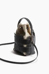 Cartera bombonera de cuero sintético color beige con apliques de tiras de cuero sintético negro y costuras blancas. Tiene doble asa corta y correa larga extraíble. El interior es de lona con cordón ajustable.