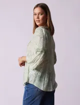 Blusa de gasa estampada color salmón con flores blancas, marca Ruby Rd. Cuello a la base, escote en V y abertura central con botones. Delantera con plisados. Largo de manga ¾ con terminación amplia.