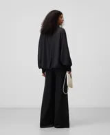 Camisa blanca de manga larga, con cuello chimenea alto y botonadura frontal oculta. El tejido es semitransparente y presenta una textura ligera.