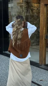 Chaleco marrón de cuero descarne con terminación en picos, tachas metálicas y flecos en la espalda.