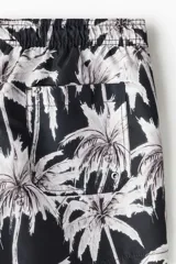 Short de baño negro con estampado de palmeras blancas, cintura elástica con cordón ajustable, bolsillos laterales y trasero.