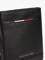 Bandolera negra de Tommy Hilfiger con acabado granulado, correa ajustable de tejido trenzado, bolsillo exterior abierto, cinta distintiva y logo metálico.