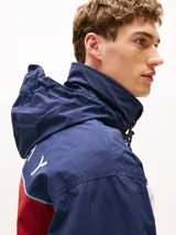 Campera náutica amplia reversible de nailon, con diseño color block en rojo, blanco y azul marino. Tiene capucha fija, cierre de cremallera oculto con botones a presión, puños y bajo elásticos, dos bolsillos ribeteados en la cintura, parche con logo de Tommy Hilfiger en el pecho y logo de Tommy Hilfiger en el cuello, las mangas y la espalda.