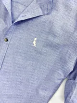 Camisa celeste con cuello mao, de manga larga con puños arremangados, cierre con botones a tono y logo bordado en el pecho.