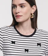 Blusa de media malla a rayas horizontales blancas y negras, con cuello redondo y mangas cortas. Aplicación de moñas negras.