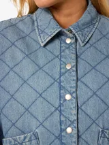 Chaqueta acolchada de denim celeste con cuello clásico y mangas largas. Cierre con broches a presión, bolsillos frontales y forro interior completo.