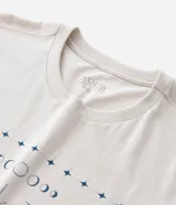 Remera color beige de corte alargado, cuello redondo y mangas cortas. Estampado frontal con una mariposa azul rodeada de elementos celestiales.