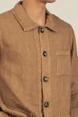 Campera color marrón claro estilo sobrecamisa confeccionada en lino premium. Cuenta con cuello clásico, cierre frontal con botones, un bolsillo de parche en el pecho y dos bolsillos de parche en la parte inferior.