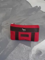 Sobre tipo cartuchera color borgoña, de lona con terminaciones en cuero marrón. Tiene cierre superior y aplique de cuero con el logo de la marca.