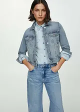 Chaqueta de jean celeste de corte clásico, con cuello camisero, cierre frontal con botones metálicos, bolsillos delanteros con solapa y puños abotonados.