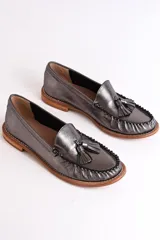 Mocasines plateados de cuero con detalle de borlas y costuras en contraste.