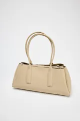 Bolso tipo tote color beige, con doble asa corta y cierre superior con botón imantado. Incluye un compartimento interno con cierre de cremallera.
