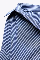 Camisa oversize a rayas verticales azules y blancas, de popelín, con cuello solapa, manga larga tipo murciélago acabada en puño con hombro caído, bolsillo de plastrón en delantero y cierre frontal con botones.