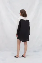 Camisa larga de lino color beige, con cuello camisero y cierre frontal con botones. Tiene mangas largas con puños abotonados, bolsillos laterales y una franja a contratono en la espalda y mangas.