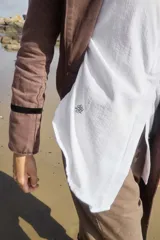 Tapado largo color marrón oscuro, con solapas anchas y cierre frontal de un solo botón. Presenta un detalle de cinta negra en la manga.