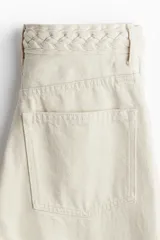 Pantalón de jean color crema, de corte amplio y cintura alta, con detalle de trenzado en la pretina.