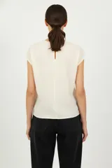 Blusa de viscosa color crudo con estampado de palmera verde, corte holgado, cuello redondo y mangas cortas.