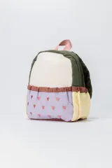 Mochila pequeña con diseño de bloques de color en tonos beige, verde oliva, lila y amarillo. Cuenta con un bolsillo frontal acolchado con estampado de pequeños corazones, cierre de cremallera y asa superior en color rosado.