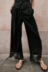 Pantalón culotte negro de tiro alto con pinzas delanteras, bolsillos frontales y falsos bolsillos de vivo en la espalda. Presenta pernera ancha y corta con bordados florales a tono en el ruedo. Cierre frontal con cremallera, botón interior y gancho.