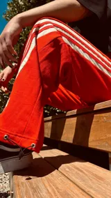 Pantalón de jogging color gris claro con cordón ajustable en la cintura y tres rayas verticales negras a los costados.