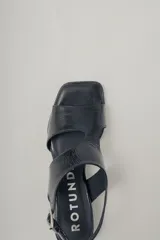 Sandalia de cuero con acabado brillante color marrón rojizo, taco ancho de altura media y punta cuadrada. Presenta tiras anchas cruzadas en el empeine y tira fina con hebilla ajustable en el tobillo.