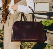 Bolso tipo tote de cuero negro con textura tipo piel de cocodrilo, doble asa de mano y cierre superior con cremallera.