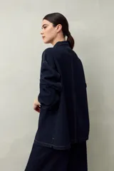 Sobrecamisa oversize de jean azul con cuello camisero, cierre frontal con botones, mangas largas y bolsillos de parche en el pecho.