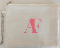 Sobre pequeño de tela color crudo con cierre superior y cadena metálica. Estampado frontal con las iniciales 'AF' en color rosa.