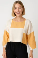 Blusa corta con diseño geométrico en tonos beige y mostaza, de corte holgado y mangas 3/4.