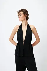 Top halter negro con escote profundo y destellos metalizados. El frunce frontal realza la silueta y el tajo sutil aporta un toque atrevido.