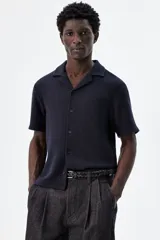 Camisa azul marino de manga corta en tejido de punto con textura. Tiene cuello resort, tapeta con botones y corte recto.