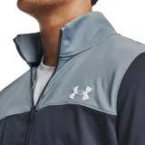 Conjunto deportivo Under Armour de hombre, compuesto por campera con cierre y pantalón largo. La campera es de color gris en la parte superior y azul marino en la parte inferior, con logo de la marca en el pecho. El pantalón es azul marino con logo de la marca en la pierna.
