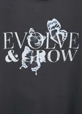 Remera negra de algodón con cuello redondo y mangas cortas. Estampado frontal con la frase "Evolve & Grow" y diseño de mariposas en color blanco.