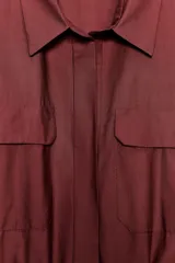 Vestido midi camisero color ladrillo, confeccionado en popelina de algodón. Presenta cuello solapa, manga corta con puños abotonados, bolsillos laterales ocultos y bolsillos de parche con solapa en el pecho. Incluye cinturón lazada en el mismo tejido y cierre frontal con botones ocultos.