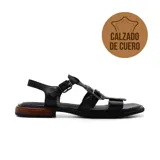 Sandalias bajas de cuero negro con tiras anchas y hebillas plateadas. La suela es plana con detalle de madera en el talón.