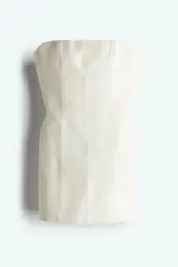 Vestido mini strapless color crudo, confeccionado en sarga de mezcla de algodón con costuras visibles y cuerpo ceñido con varillas. Presenta cintura interior de grosgrain con cierre ajustable de corchete, cierre oculto con cierre de corchete en la espalda y cadera sobredimensionada. Forrado.