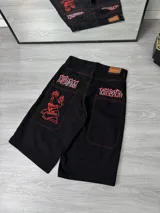 Bermuda negra de corte ancho con costuras rojas contrastantes, bolsillos traseros y laterales. Presenta un estampado de graffiti en rojo en los bolsillos traseros y en el lateral de una pierna.