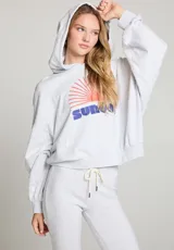 Hoodie gris jaspeado con capucha y mangas amplias. Estampado frontal con la palabra "Sunday" en azul y un sol naciente en naranja.