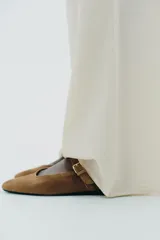 Zapato plano tipo bailarina en serraje color marrón. Escote redondo y cierre mediante hebilla en el empeine.