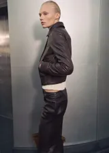 Chaqueta bomber de cuero color marrón oscuro con cuello camisero y cierre frontal con cremallera y botones a presión. Tiene terminaciones elásticas en puños y cintura, y dos bolsillos laterales.