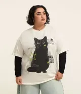 Remera de algodón color crudo, de corte holgado y mangas cortas. Estampado frontal con un gato negro y detalles gráficos en verde y negro.