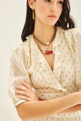 Top corto cruzado color crema con estampado de puntos dorados, escote en V con volados y mangas abullonadas al codo con puños elastizados.