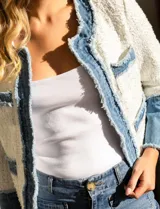 Chaqueta Nanette en tejido tweed color blanco y denim azul. Tiene cuello a la base, abertura central, bolsillos delanteros, puños con aplique de botones perlados, terminación desflecada y forro interno.