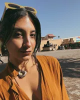 Collar con dije dorado irregular con agujero central, colgando de cordón negro ajustable.