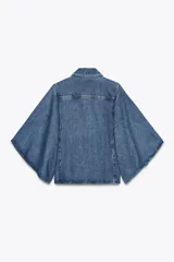 Camisa de denim azul con cuello solapa y mangas amplias tipo kimono. Tiene efecto lavado y cierre frontal con botones ocultos.