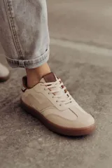 Zapatillas urbanas color crema, confeccionadas en cuero, con suela de goma color caramelo y cordones al tono.