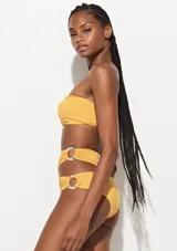 Bikini amarillo mostaza de dos piezas marca Triya. El corpiño es strapless y la bombacha es de tiro alto con aberturas laterales unidas por argollas con estampado floral.