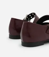 Zapatilla color borgoña de charol sintético, con puntera redonda, tira sobre el empeine con hebilla metálica plateada y taco bajo.