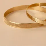 Pulsera rígida dorada con textura satinada y otra con textura martillada.