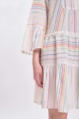 Vestido corto blanco con rayas verticales multicolor, escote en V, mangas largas acampanadas y falda escalonada con volantes.